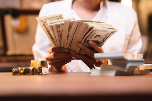 Businesswoman holding a stack of dollar bills over financial charts on a desk.