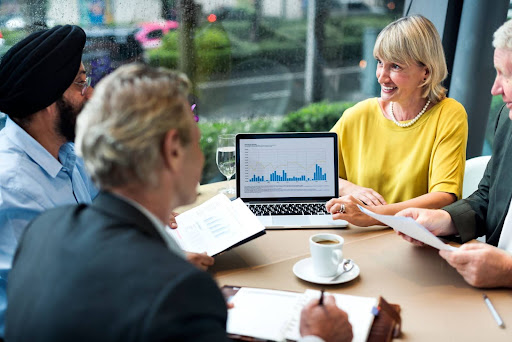 Group of business professionals discussing financial charts during a meeting with a laptop displaying graphs.