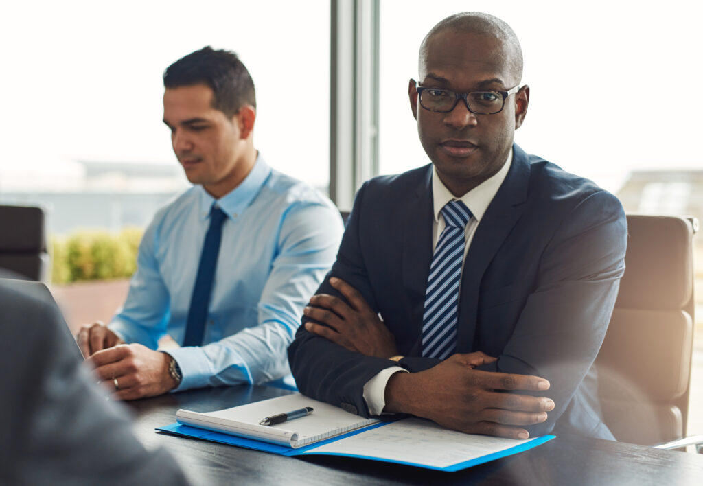 Executive multiracial business team having a meeting in the office with focus to a serious middle-aged African American man looking at the camera with folded arms