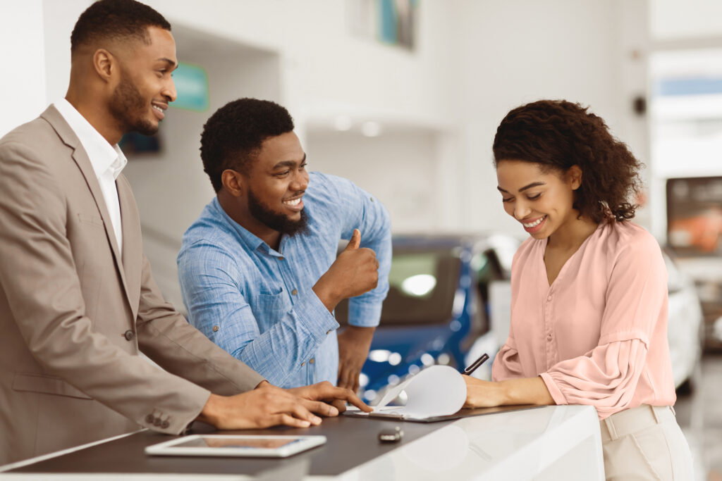 Couple Signing Papers With Car Dealer Buying Auto In Dealership