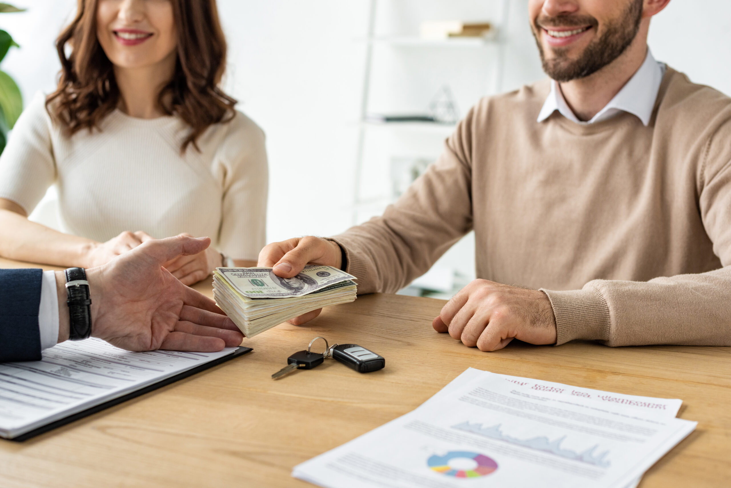 cropped view of happy man giving dollar banknotes to car dealer near cheerful woman