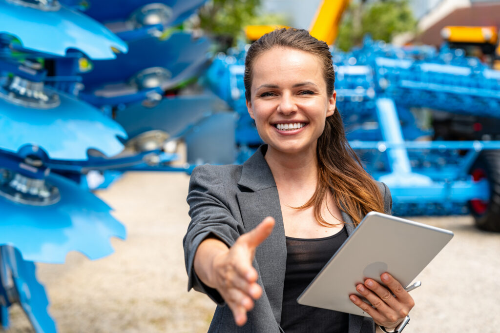 Female agricultural sales representative offering handshake at outdoor equipment dealership